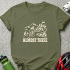 Olive green t-shirt featuring a cream graphic of a cyclist climbing a mountain and the text ALMOST THERE.