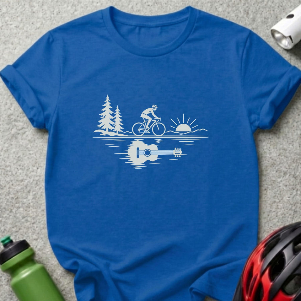 A blue t-shirt with a white graphic showing a cyclist, trees, sun, and an acoustic guitar reflection.