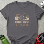 T-shirt with graphic of coffee cup, bike wheel, road, and mountains. Text reads "Coffee First. Miles Next."