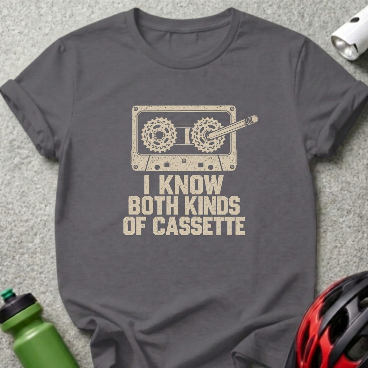 Charcoal grey t-shirt featuring a cassette tape graphic with bicycle gears and the text I KNOW BOTH KINDS OF CASSETTE.