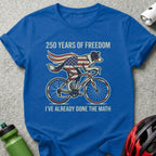 Blue t-shirt with dog on a bicycle, American flag cape, "250 Years of Freedom" and "I've Already Done the Math".