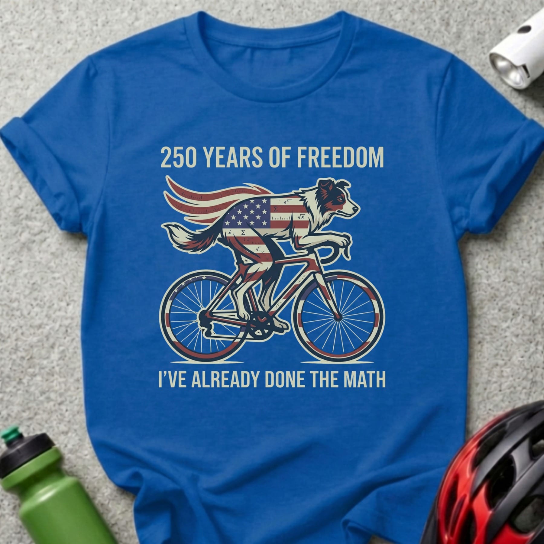 Blue t-shirt with dog on a bicycle, American flag cape, "250 Years of Freedom" and "I've Already Done the Math".