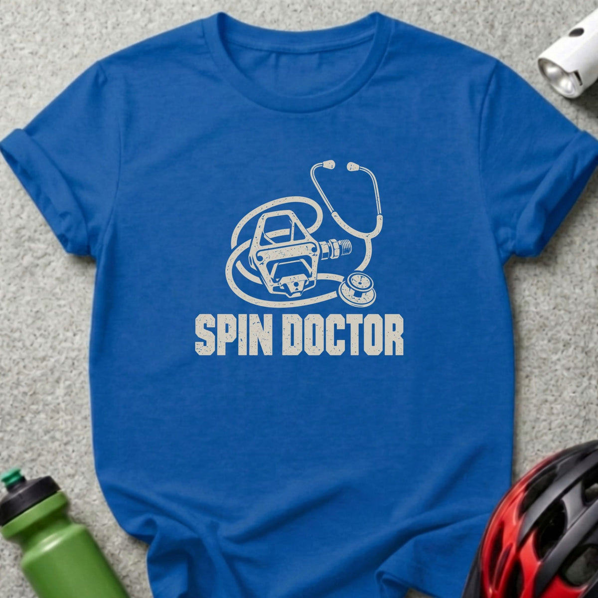A blue t-shirt featuring a white graphic of a stethoscope intertwined with a bicycle pedal above the text Spin Doctor.