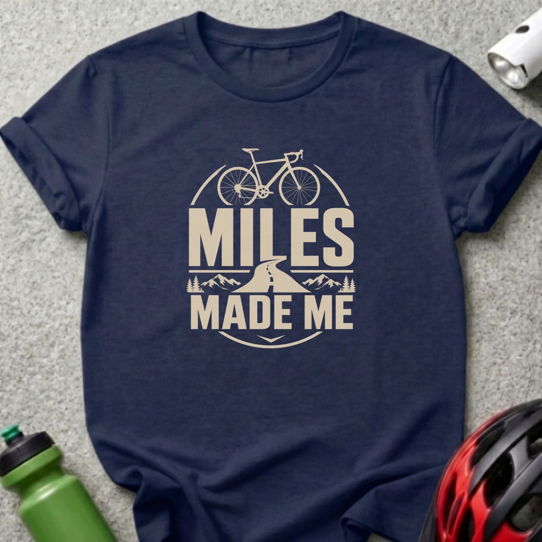Dark blue t-shirt with "MILES MADE ME" text, bicycle, road, and mountains graphic.