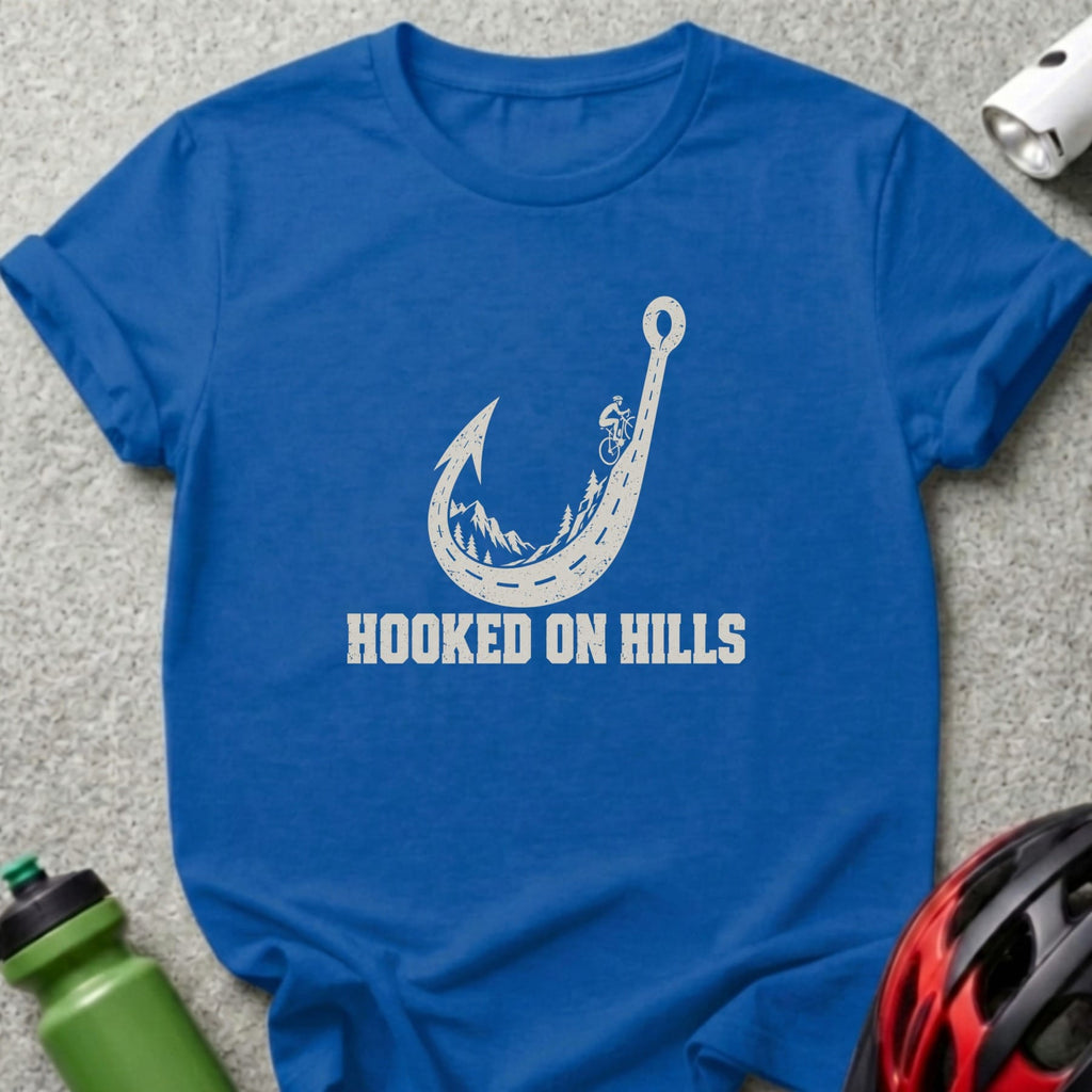 Royal blue t-shirt featuring a white graphic of a winding road shaped like a fishhook, with mountains, trees, a cyclist, and the text HOOKED ON HILLS.