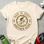 Cream t-shirt with "Age is just another gear" cycling graphic.
