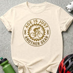 Cream t-shirt with "Age is just another gear" text and cyclist graphic.