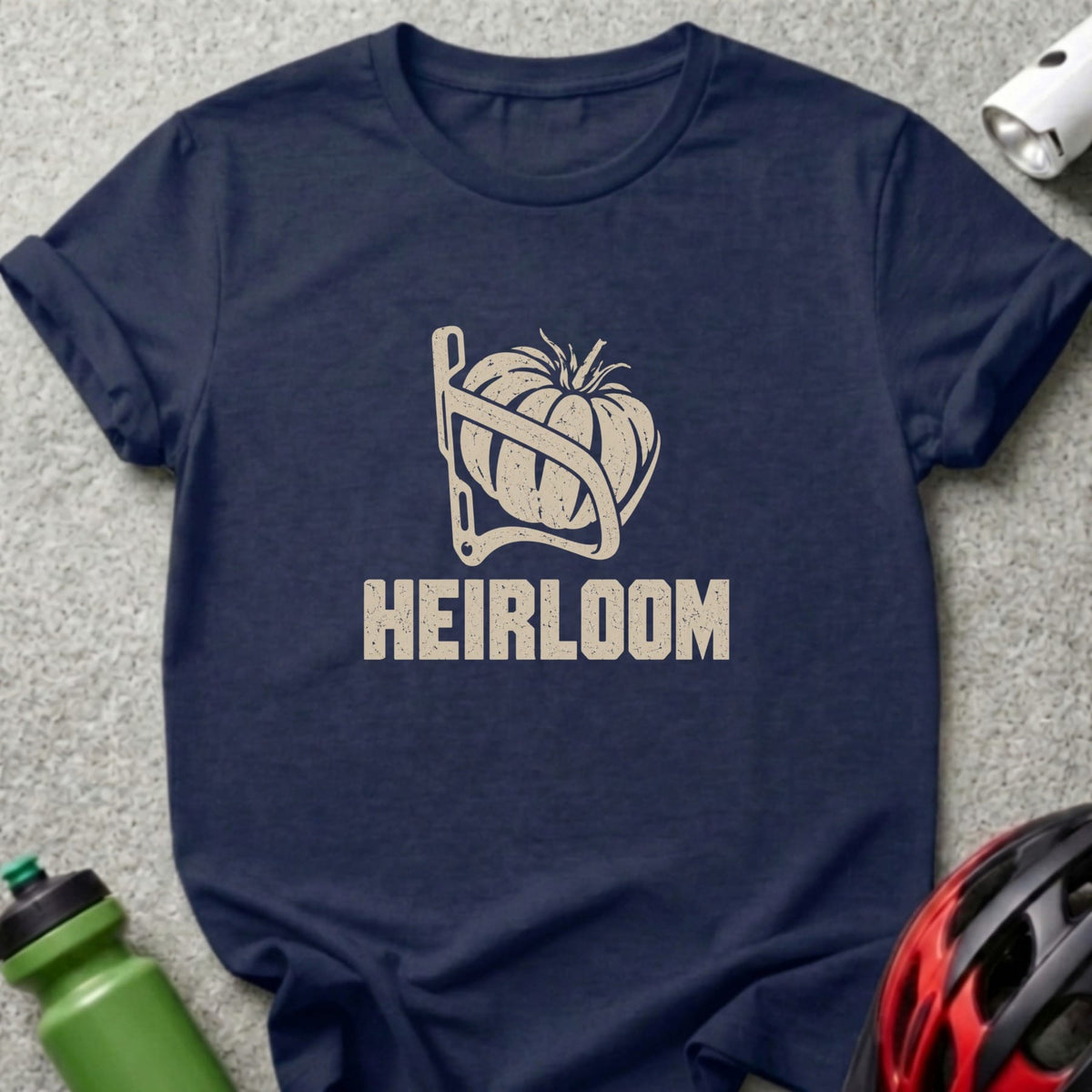 A dark blue t-shirt with a beige graphic of a tomato in a bicycle water bottle cage and the text HEIRLOOM.