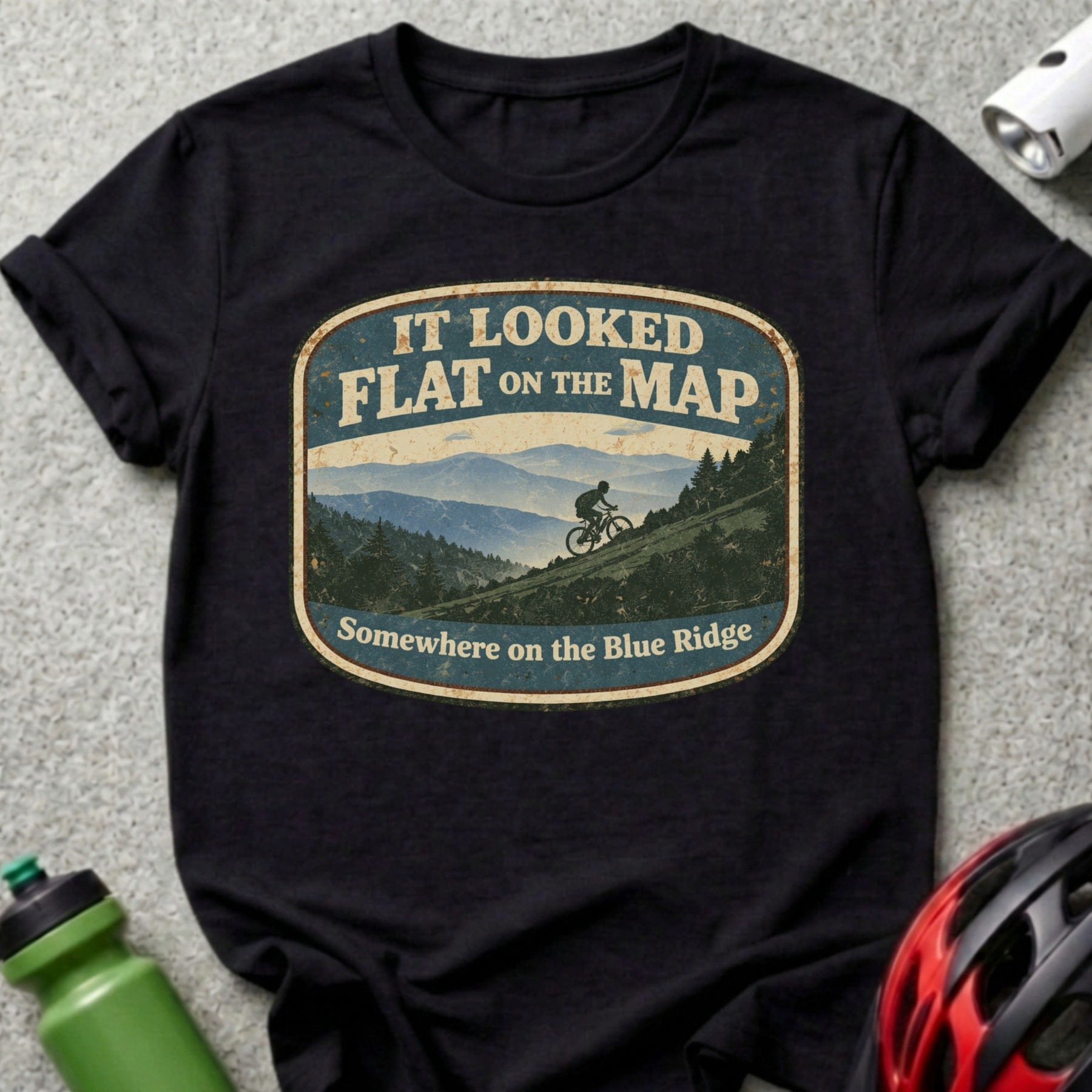 T-shirt with oval graphic of cyclist on mountain path, "It looked flat on the map" text.