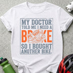 White t-shirt with text "MY DOCTOR TOLD ME I NEED A BRAKE SO I BOUGHT ANOTHER BIKE" and bike brake graphic.
