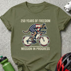 Dog wearing American flag cycling jersey on bicycle, "250 Years of Freedom Mission in Progress".
