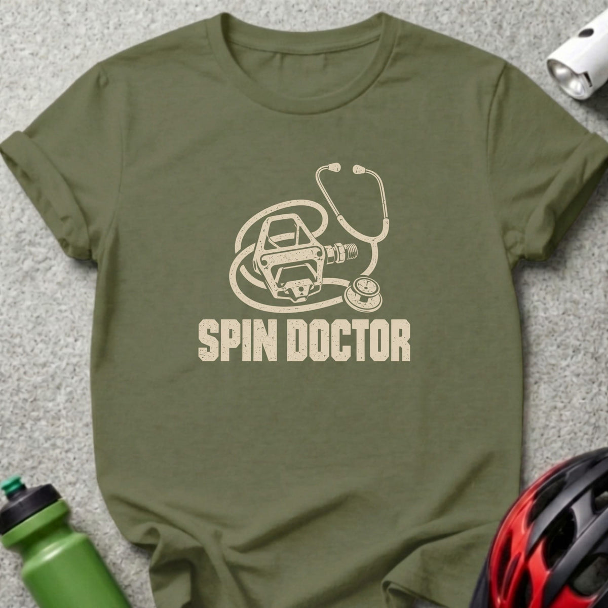 An olive green t-shirt with a graphic of a stethoscope intertwined with a bicycle pedal and the text Spin Doctor.