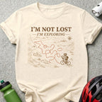 Cream t-shirt with map design and cyclist, reads "I'm not lost, I'm exploring."