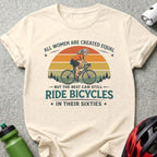 Cream t-shirt with graphic of woman cycling, text "All women are created equal but the best can still ride bicycles in their sixties".