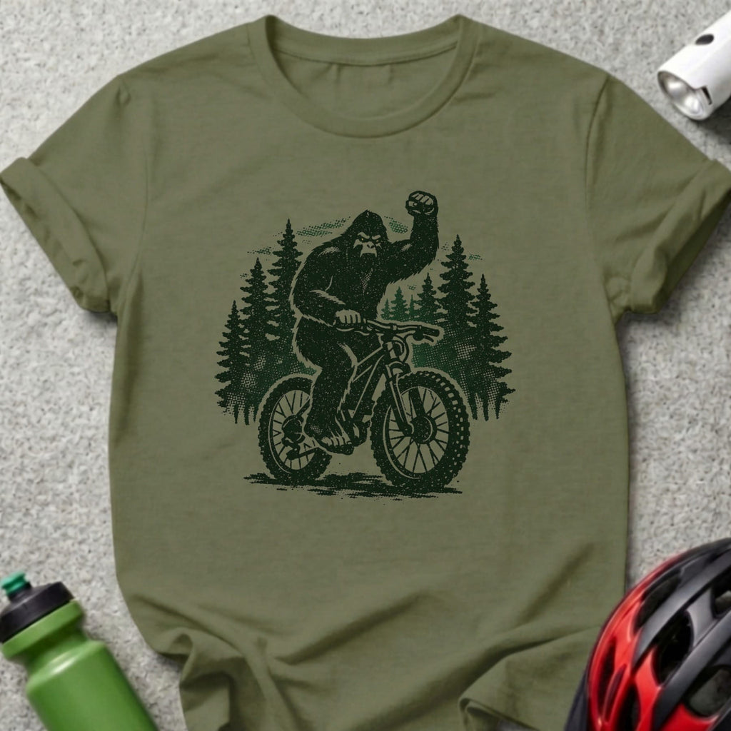 Olive t-shirt featuring a Bigfoot riding a mountain bike with trees behind it.