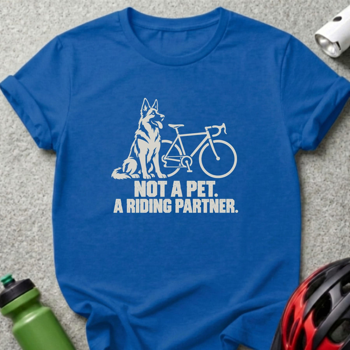 A blue t-shirt printed with a white graphic of a dog next to a bicycle and the text NOT A PET. A RIDING PARTNER.