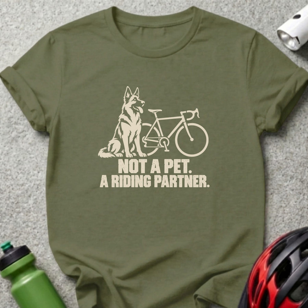 An olive green t-shirt features a white graphic of a dog next to a bicycle, with the text NOT A PET. A RIDING PARTNER.