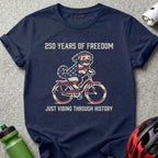 Navy t-shirt with dog riding bicycle, "250 Years of Freedom" and "Just Vibing Through History" text.