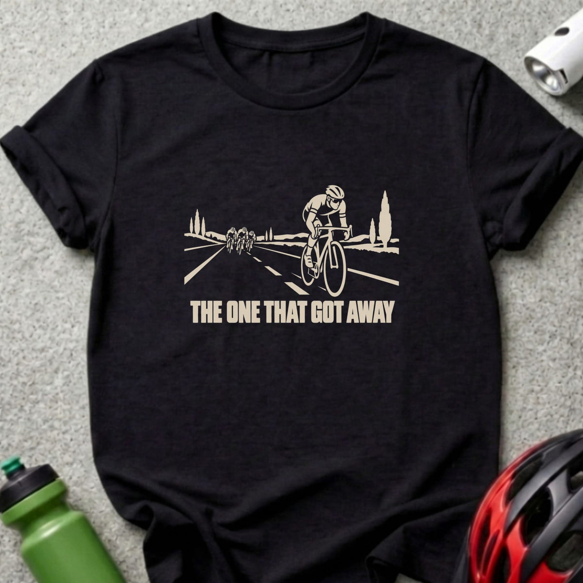 A black t-shirt printed with a graphic of cyclists on a road and text reading THE ONE THAT GOT AWAY.