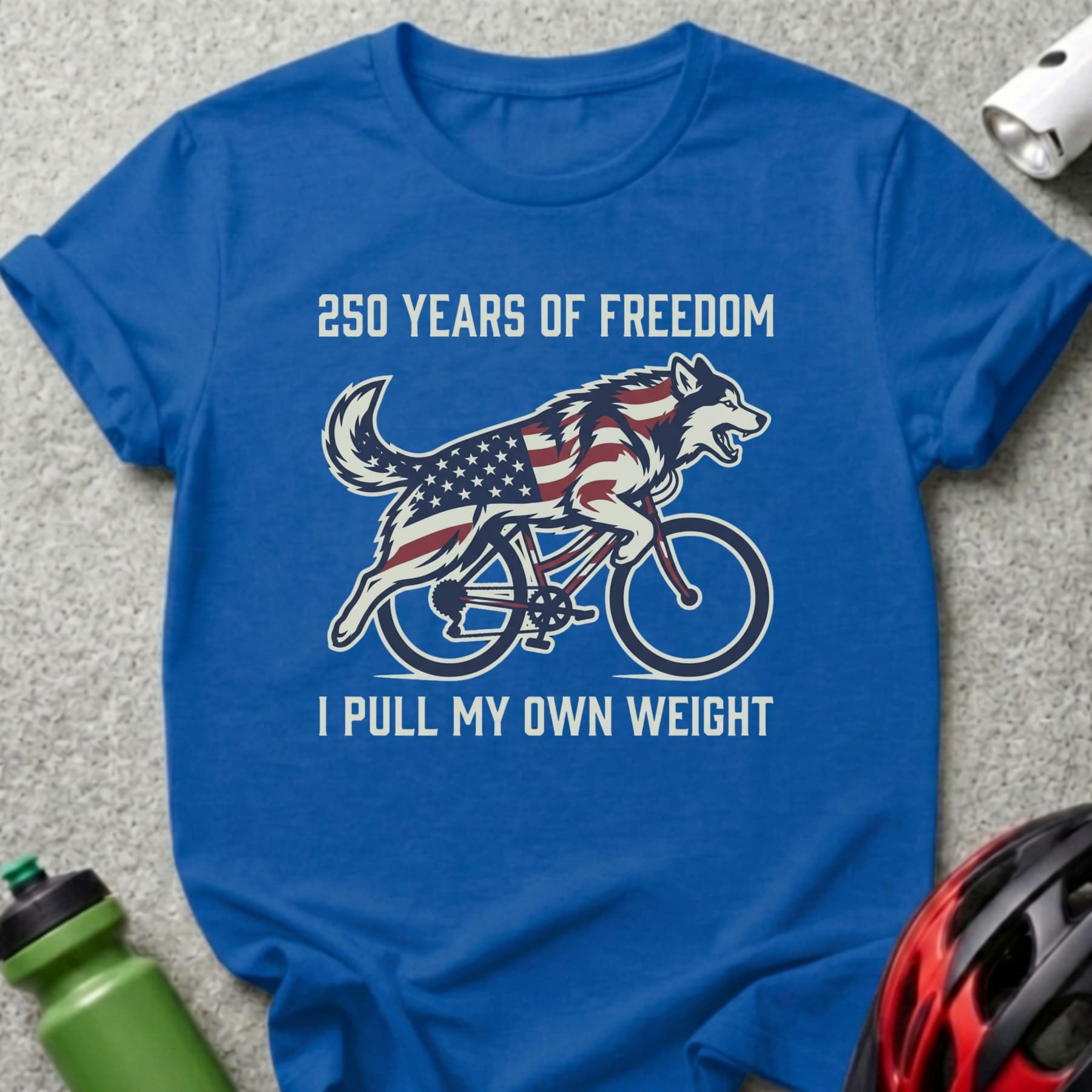 Blue t-shirt with a dog in a flag design riding a bicycle.