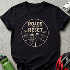 Black t-shirt with graphic: cyclist on winding road, text "ROADS ARE MY RESET".