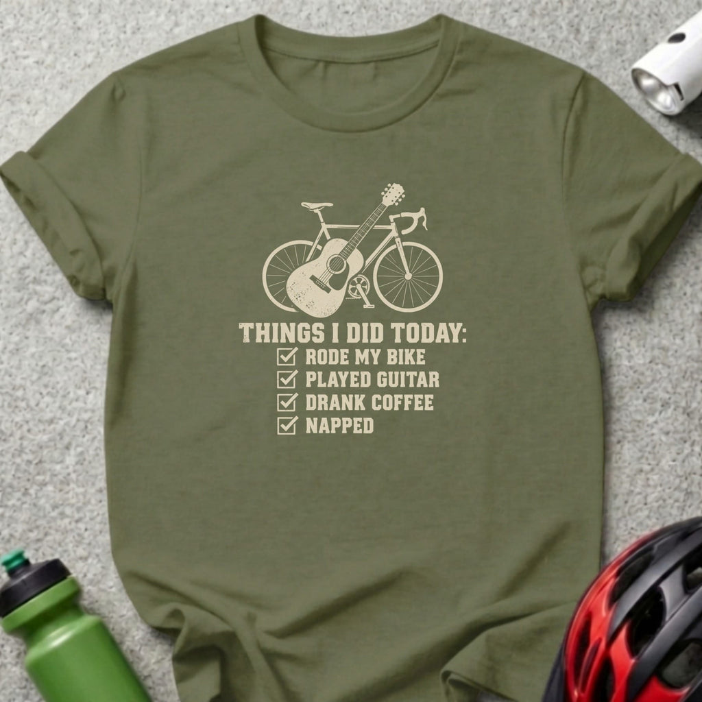 An olive green crewneck t-shirt featuring a graphic of a bicycle with an acoustic guitar and a checklist reading "THINGS I DID TODAY: RODE MY BIKE, PLAYED GUITAR, DRANK COFFEE, NAPPED".