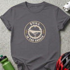 A dark gray crewneck t-shirt featuring a circular graphic with a bicycle saddle and the text Still in the Saddle.