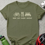 Olive green t-shirt with icons of a bicycle, fork and knife, and bed, and the text "RIDE • EAT • SLEEP • REPEAT".