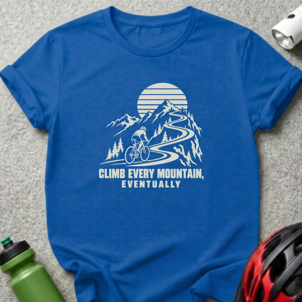 A blue t-shirt featuring a white graphic of a cyclist climbing a winding mountain road, paired with the text "CLIMB EVERY MOUNTAIN, EVENTUALLY".
