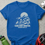 A blue t-shirt featuring a white graphic of a cyclist climbing a winding mountain road, paired with the text "CLIMB EVERY MOUNTAIN, EVENTUALLY".
