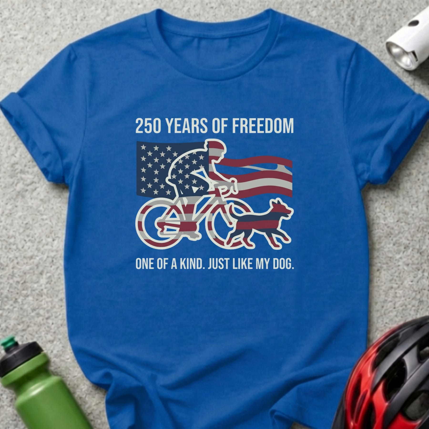 Blue t-shirt with a cyclist and dog illustration, American flag, and text.