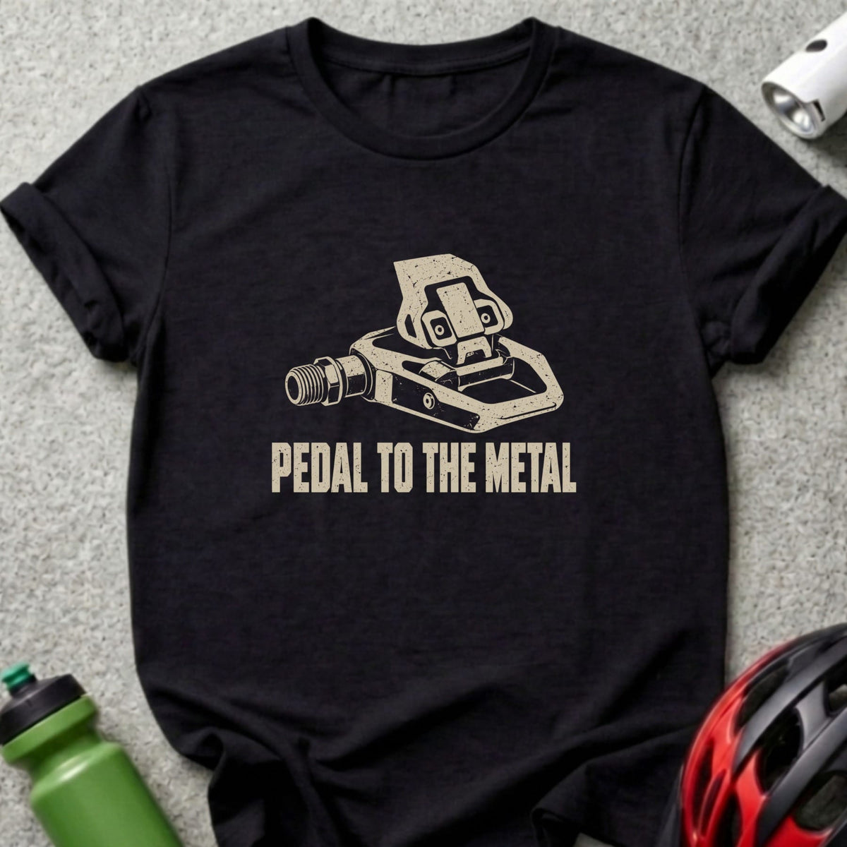 A black t-shirt printed with a graphic of a bicycle pedal and the text PEDAL TO THE METAL.
