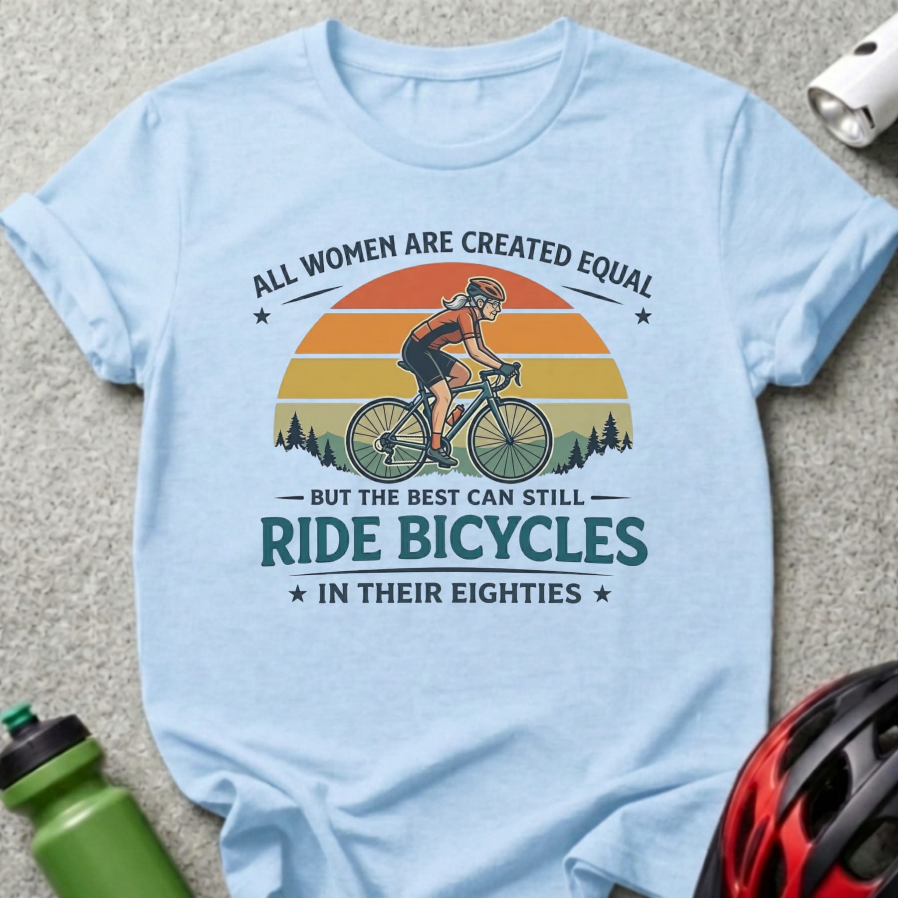 Light blue t-shirt with graphic of woman on bicycle and text "Ride Bicycles in Their Eighties".