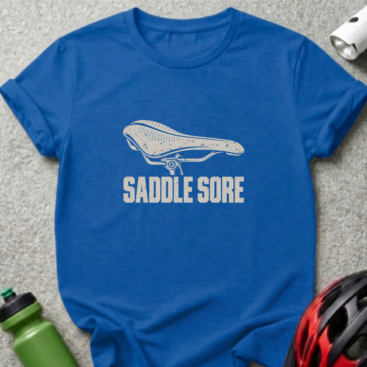 Blue t-shirt featuring a distressed white bicycle saddle graphic with the text SADDLE SORE.