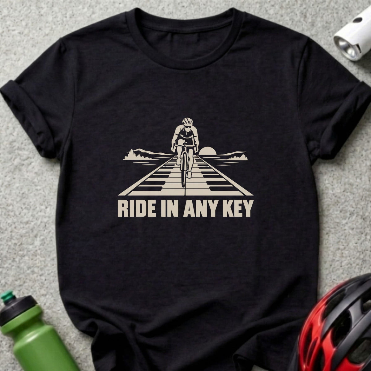 Black t-shirt featuring a graphic of a cyclist riding down a piano-key road with text reading RIDE IN ANY KEY.