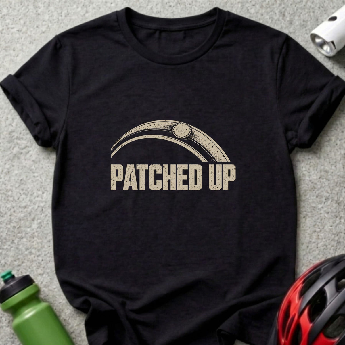 Black t-shirt featuring the beige text "PATCHED UP" under a bicycle tire graphic.