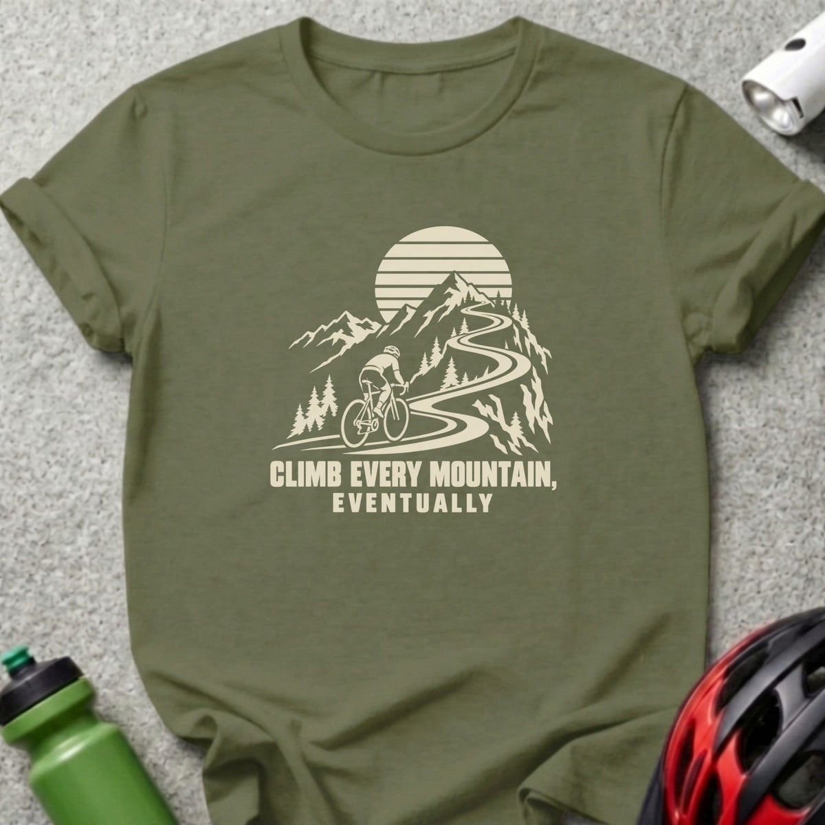 Olive green crew neck t-shirt with a graphic of a cyclist on a mountain road and text reading "CLIMB EVERY MOUNTAIN, EVENTUALLY".
