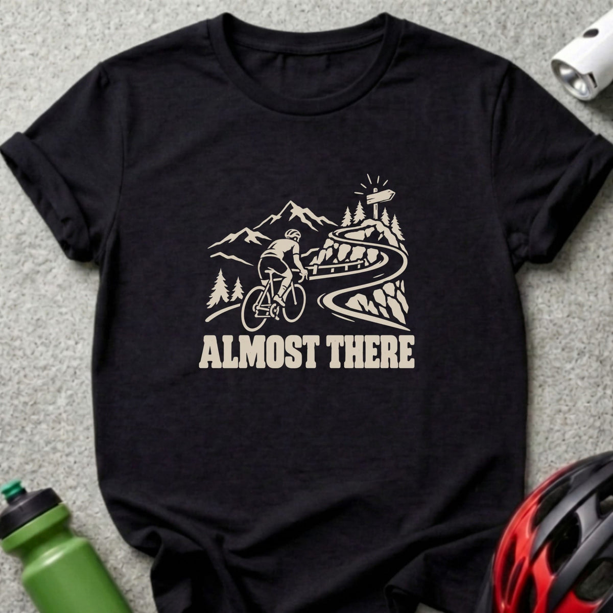 A black t-shirt features a white graphic of a cyclist on a mountain road and the text ALMOST THERE.