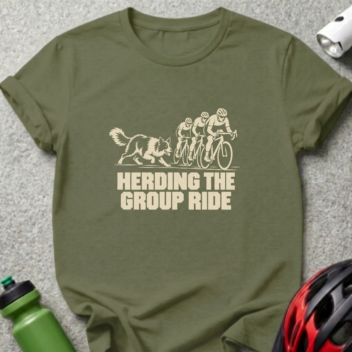 An olive green t-shirt featuring a cream graphic of a dog herding three cyclists and text reading HERDING THE GROUP RIDE.