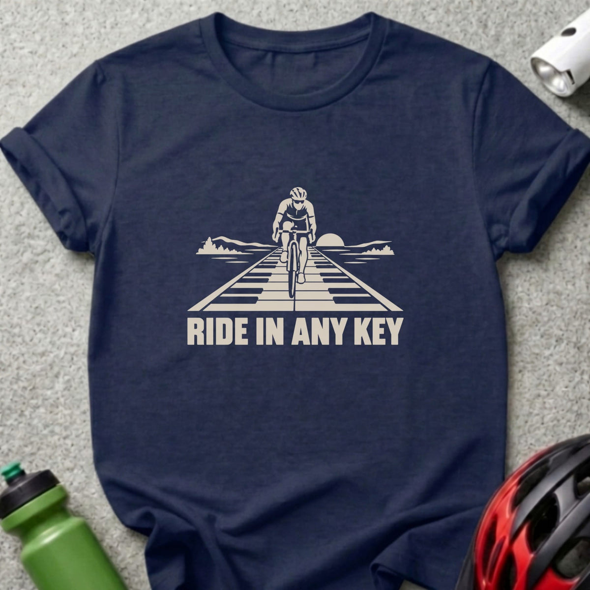 Navy blue t-shirt featuring a cyclist on a piano-key road with the text RIDE IN ANY KEY.
