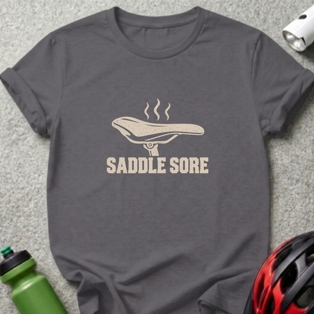 A dark grey t-shirt featuring a bicycle saddle graphic with steam and the text SADDLE SORE.