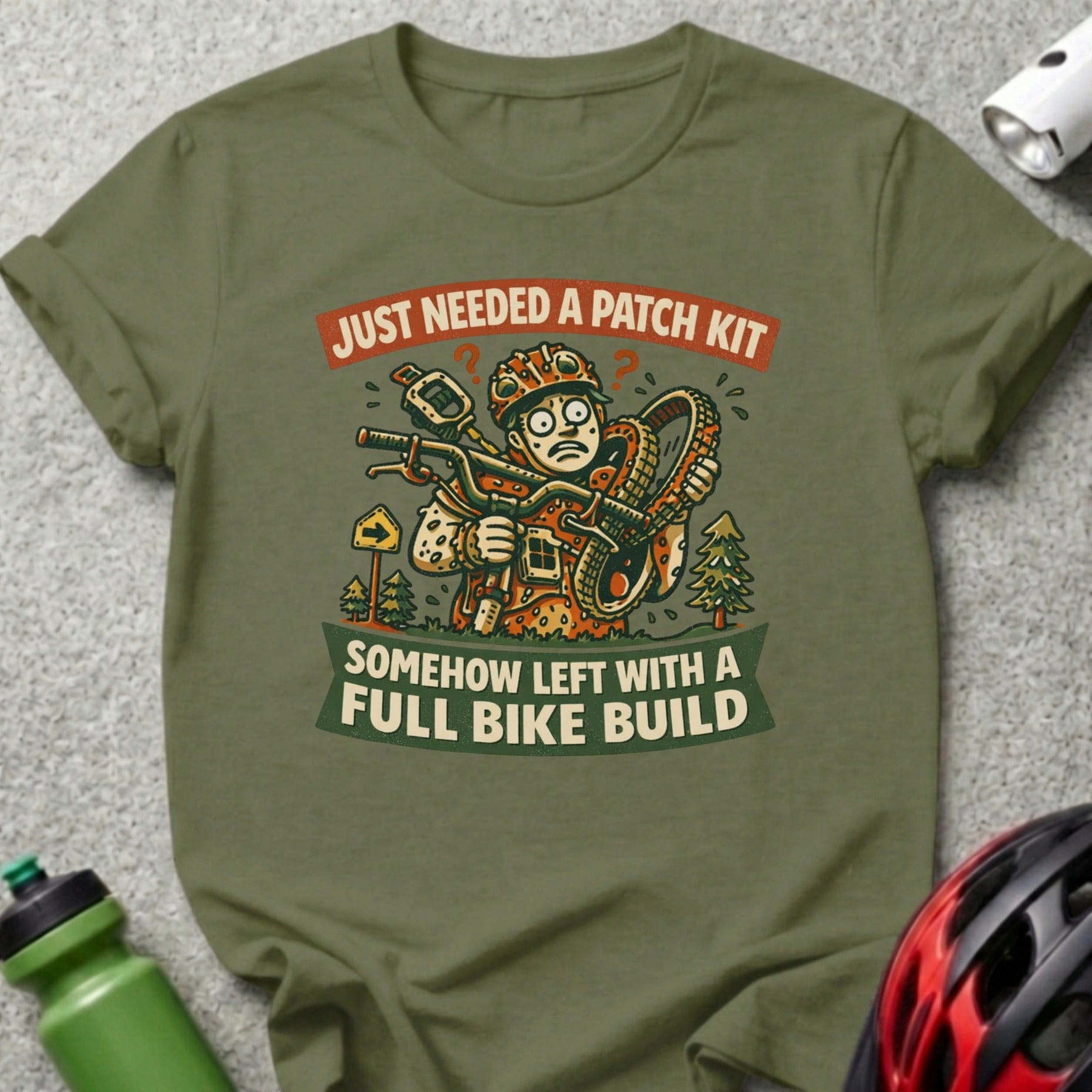 T-shirt graphic with cartoon cyclist holding flat tire, text: "Just Needed a Patch Kit, Somehow Left with a Full Bike Build".