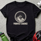 Black t-shirt featuring a graphic of a sleeping cat inside a bicycle wheel with the text PURRFECT CADENCE.