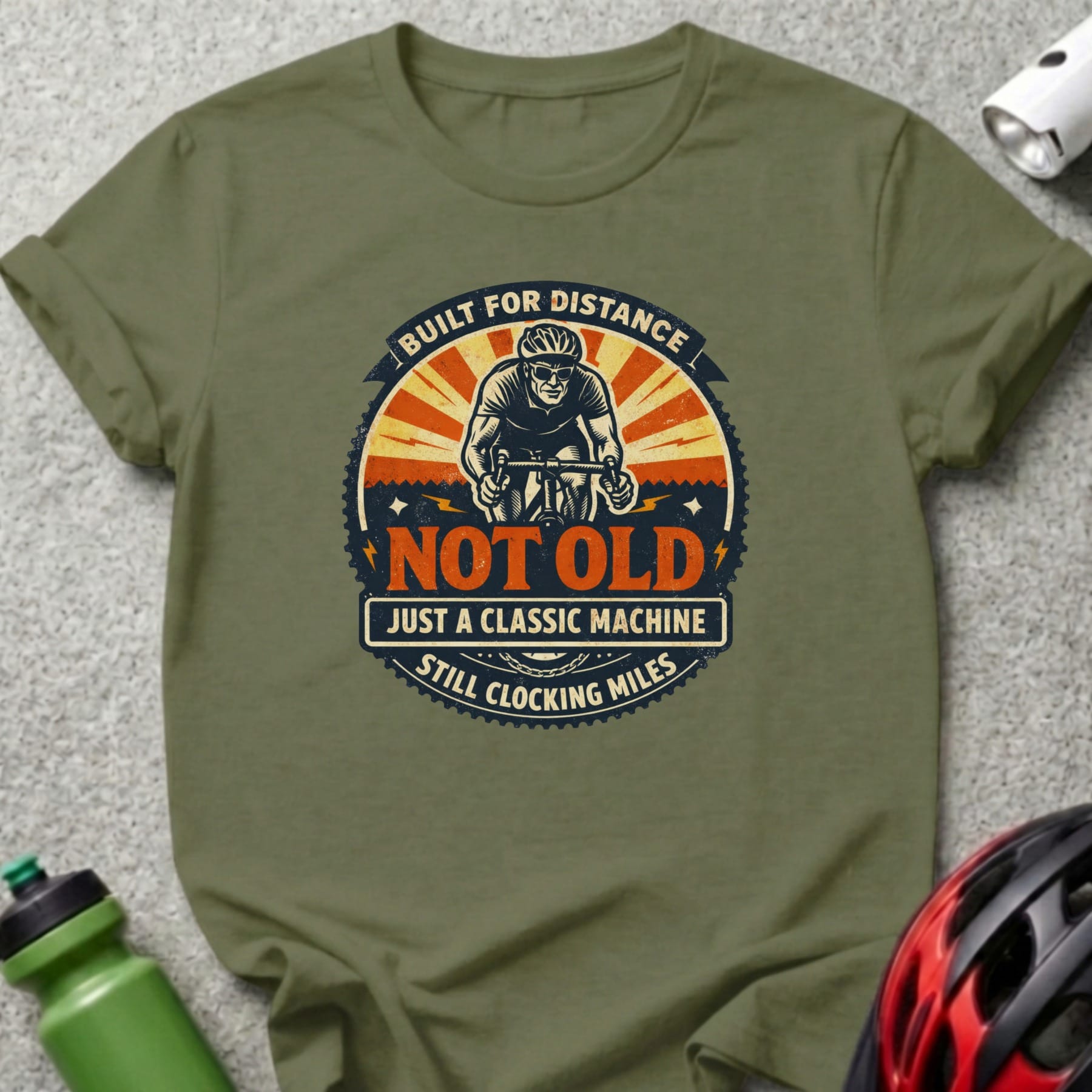 Olive green t-shirt with "Built for Distance Not Old Still Clocking Miles" cyclist graphic.