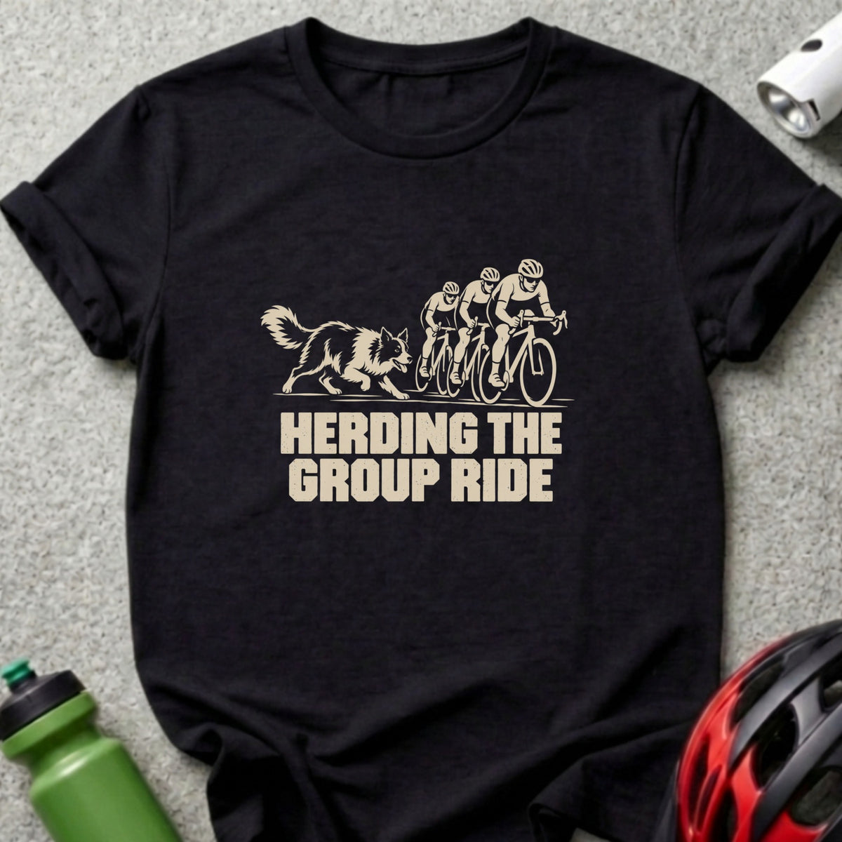 A black short-sleeved t-shirt featuring a beige graphic of cyclists and a dog with text reading HERDING THE GROUP RIDE.
