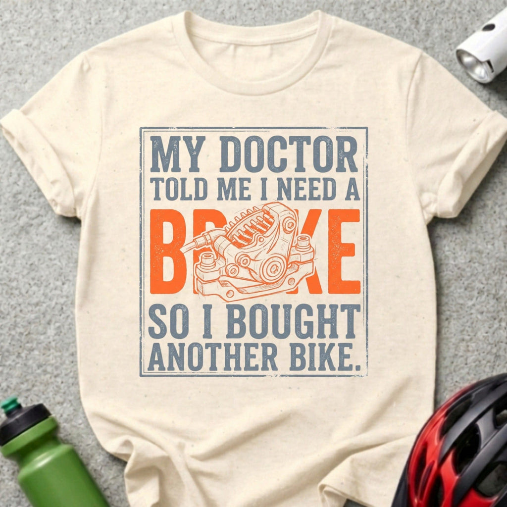 Cream t-shirt with "My doctor told me I need a brake, so I bought another bike" and bike brake graphic.