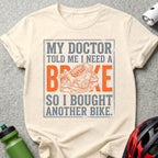 Cream t-shirt with "My doctor told me I need a brake, so I bought another bike" and bike brake graphic.