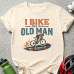 Cream t-shirt with graphic of a cyclist and text "I BIKE LIKE AN OLD MAN TRY TO KEEP UP".