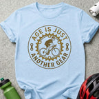Light blue t-shirt with brown circular graphic: "Age is just another gear" and cyclist.