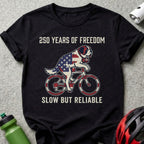 Black t-shirt with a St. Bernard on a bicycle, USA flag design, "250 Years of Freedom, Slow but Reliable".